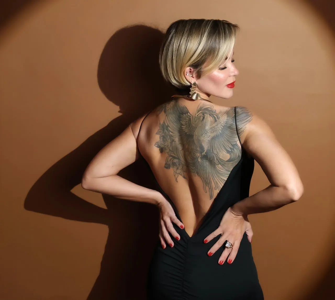 Elizabeth massoterapeuta de costas em ensaio fotográfico, mostrando as costas e a tatuagem sobre fundo terracota