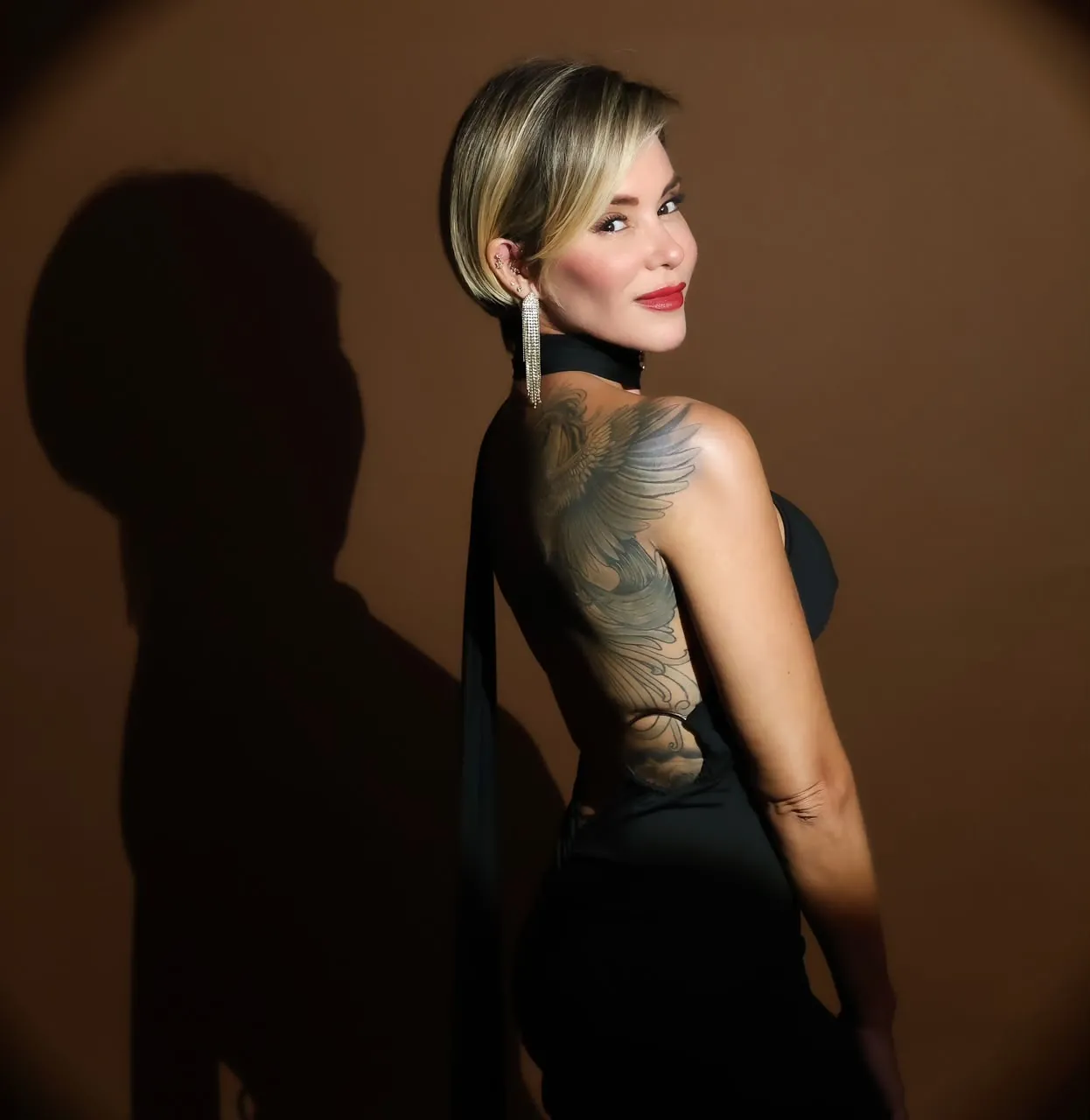 Elizabeth de perfil olhando por cima do ombro, com a tatuagem das costas visível